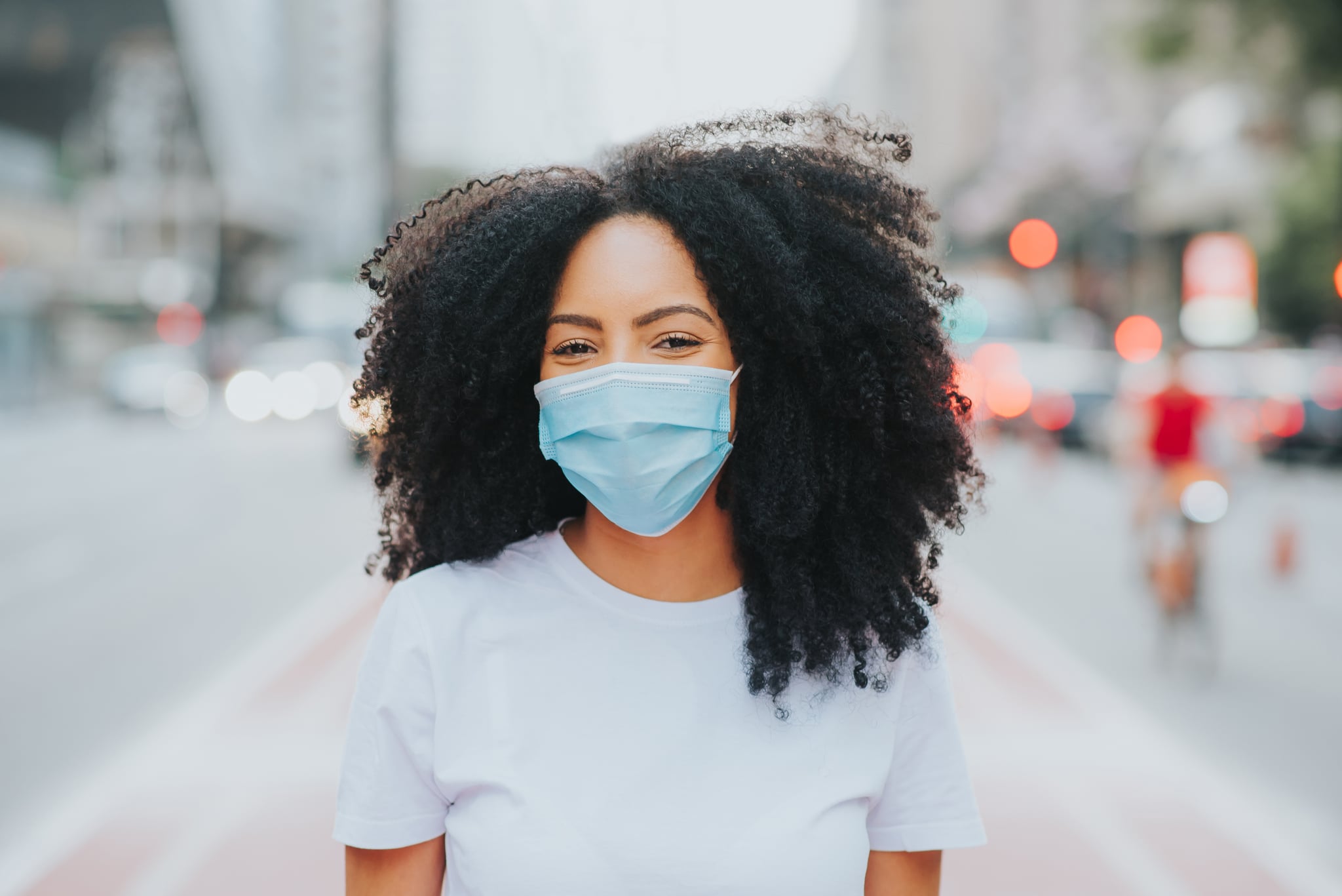 Young woman in the city smiling behind the coronavirus face protection mask