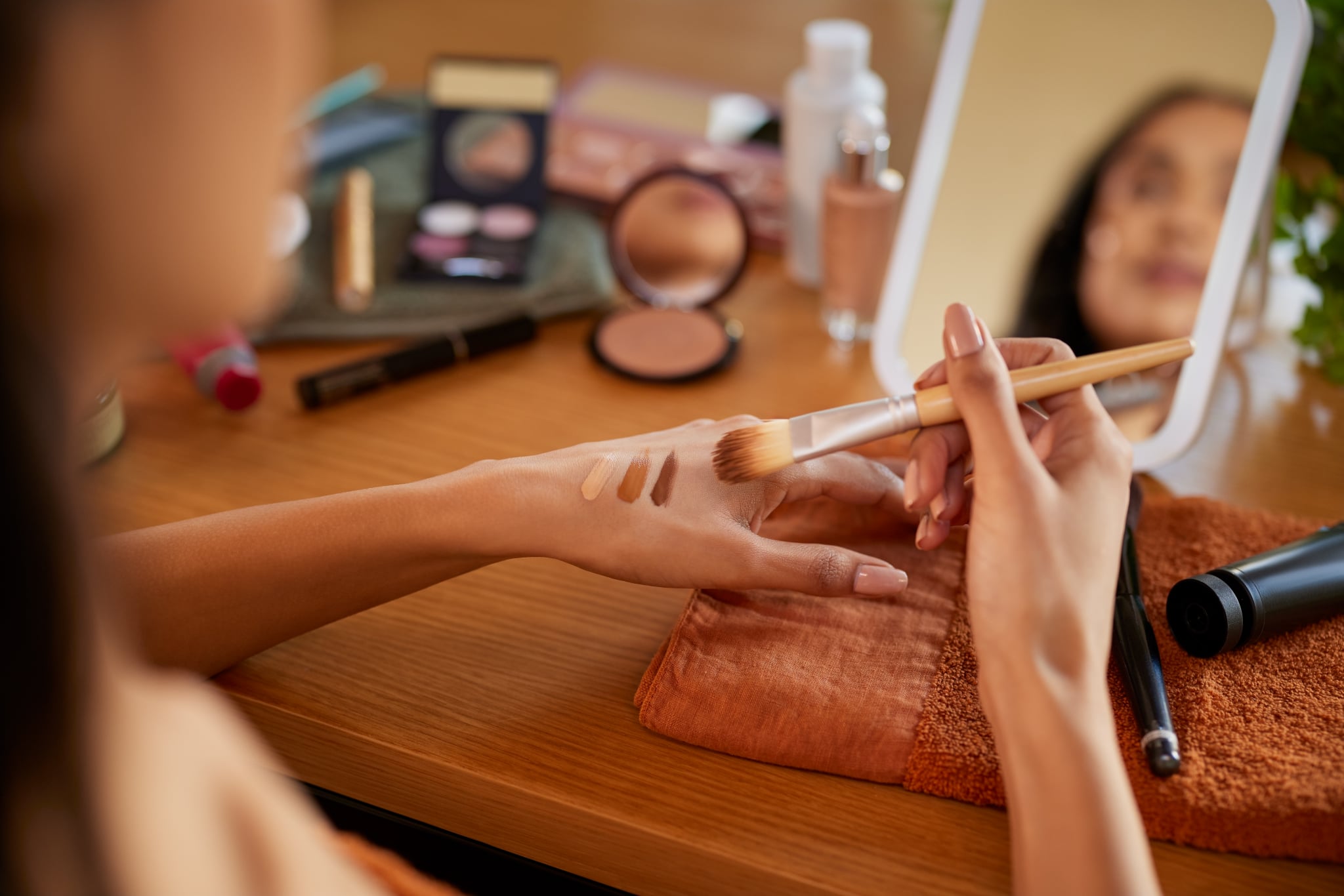 Close up of hands of young mixed race woman applying different shades of foundation on hand before makeup. Latin girl testing skin tone complexion on hand. Detail hands of mexican woman applying liquid foundation and mixing colours while preparing for the date.