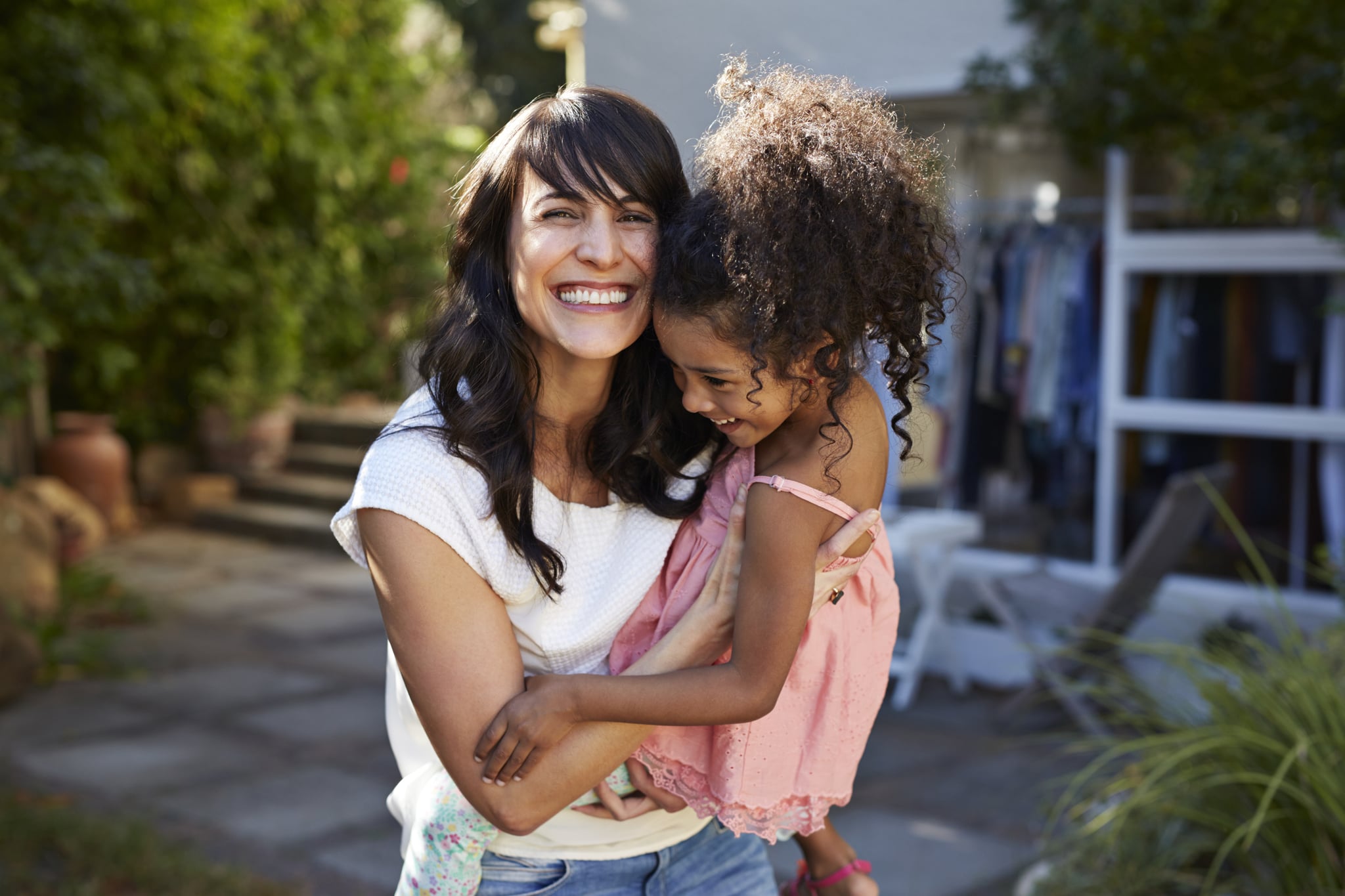 Mother carrying daughter & both laughing in garden