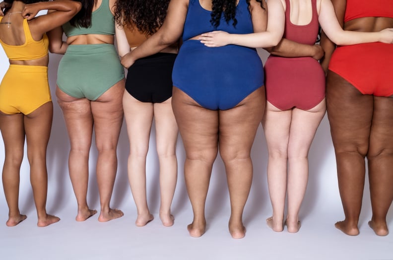 Rear view of group of women with different body type in underwear standing together on white background. Cropped shot of diverse females in lingerie with their arms around each other.