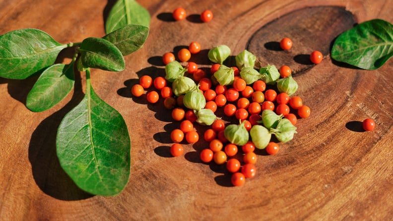 Ashwagandha leaves and red fruit berries on wooden background.