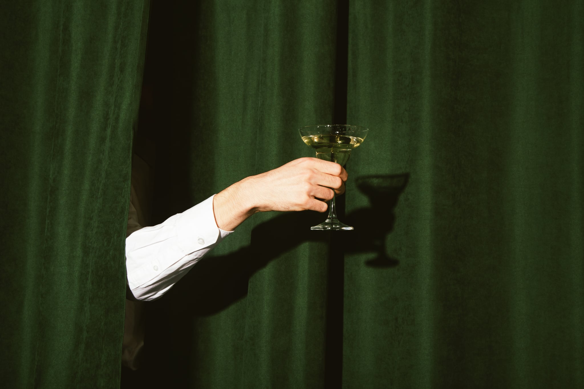 Hand with a martini glass sticks out from the green curtains