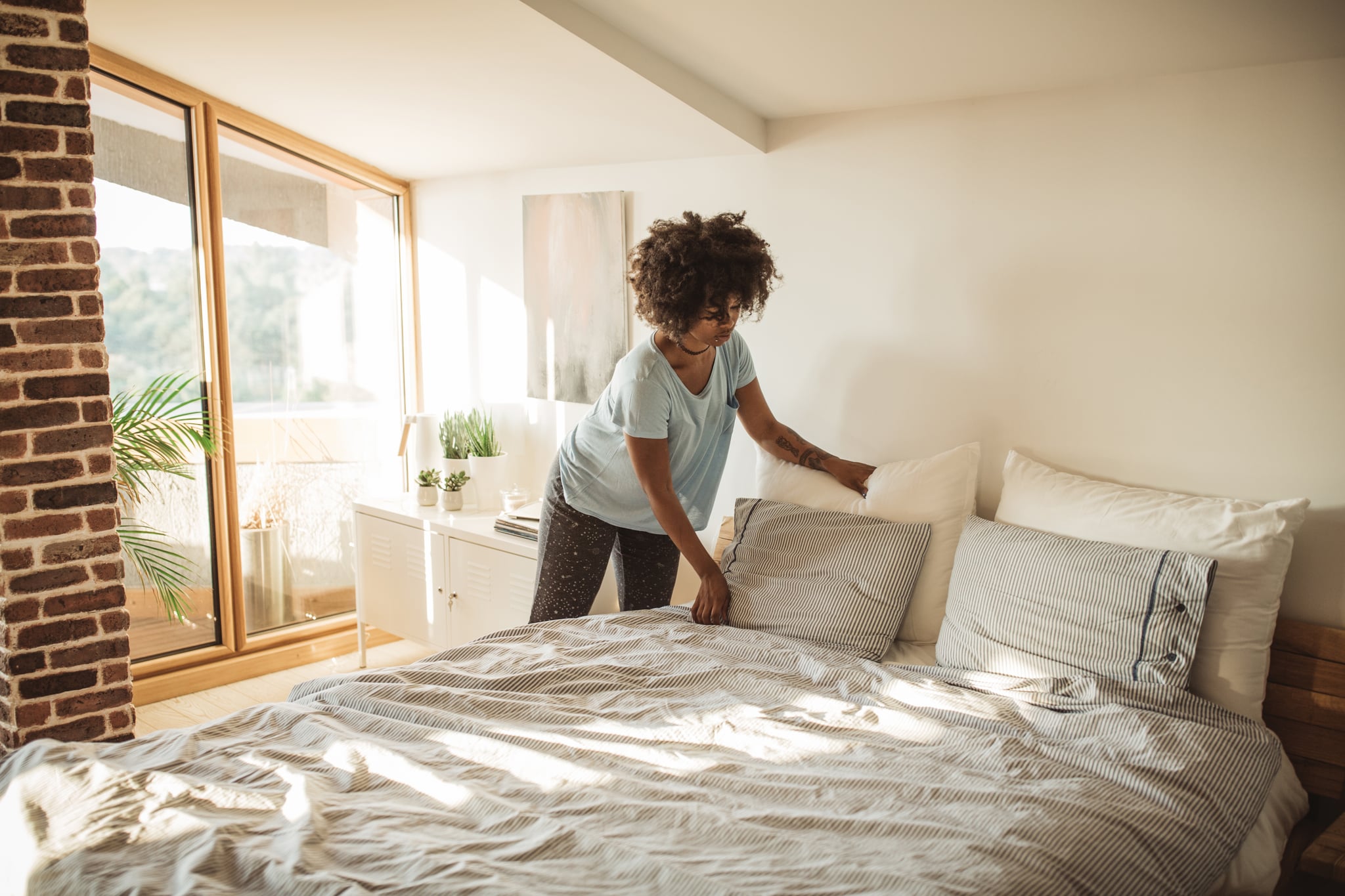 Young woman making her bed at home.