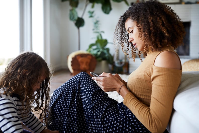 co-parenting mom looking at her phone while sitting next to her daughter