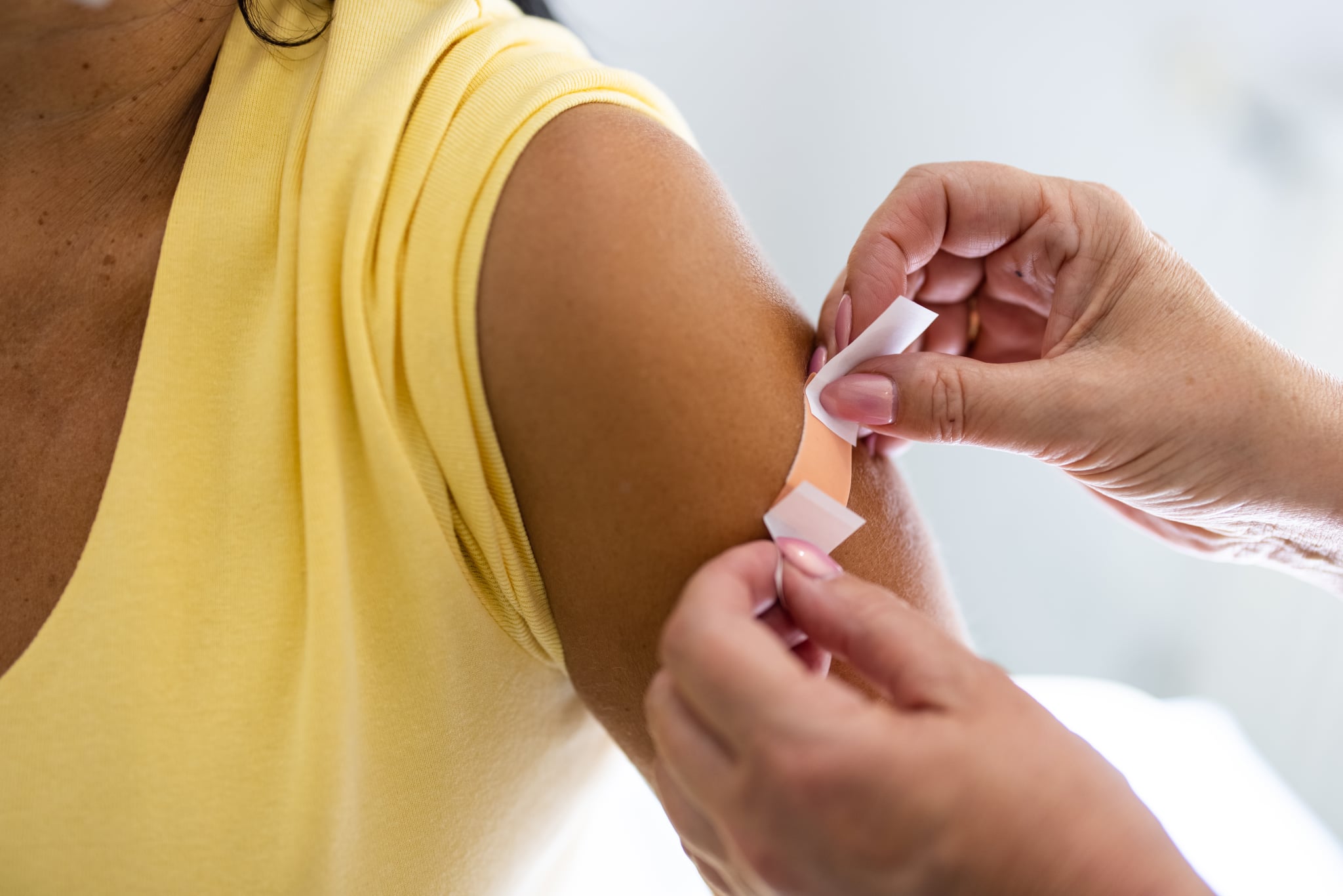 特写镜头的女医生给一个女人的手臂创可贴给疫苗注射后在诊所。医疗专业的手把女性的手臂上的绷带后covid-19接种疫苗。