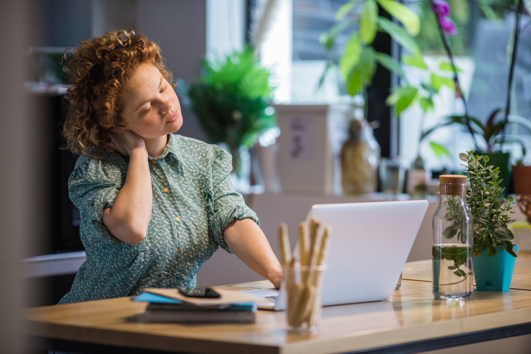 Young exhausted woman holding her neck while working on a computer at home.