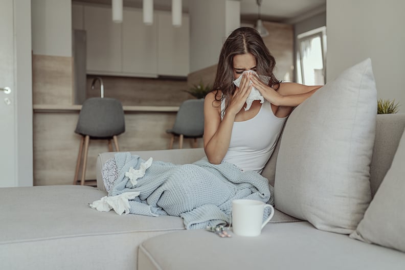 Sick Woman Covered With a Blanket Lying in Bed With High Fever and a Flu, Resting at Living Room. She Is Exhausted and Suffering From Flu. Sick Woman With Runny Nose Lying in Bed. Girl Suffering From Cold Lying in Bed With Tissue Blowing Her Nose While Si