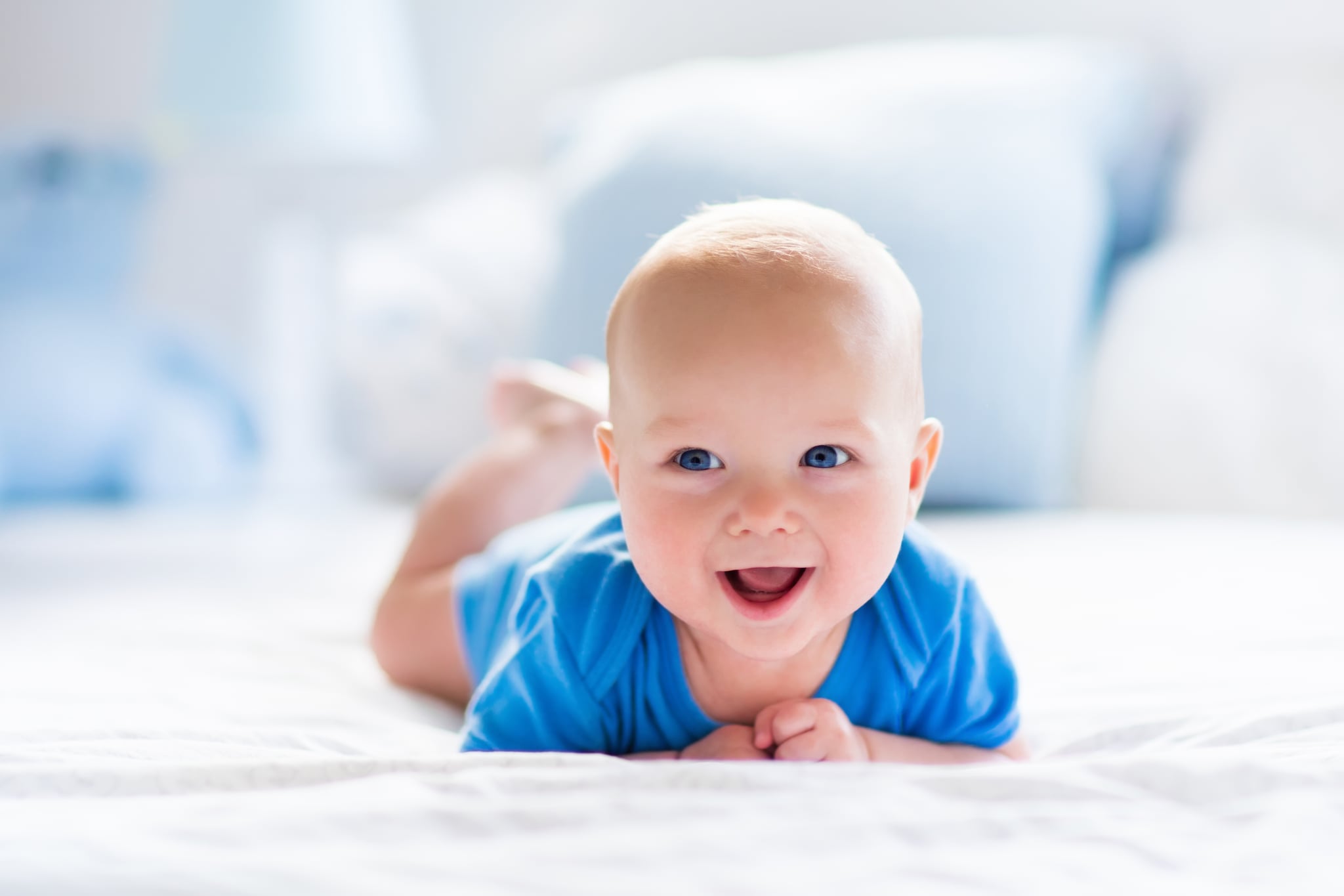 Adorable baby boy in white sunny bedroom. Newborn child relaxing in bed. Nursery for young children. Textile and bedding for kids. Family morning at home. New born kid during tummy time with toy bear.