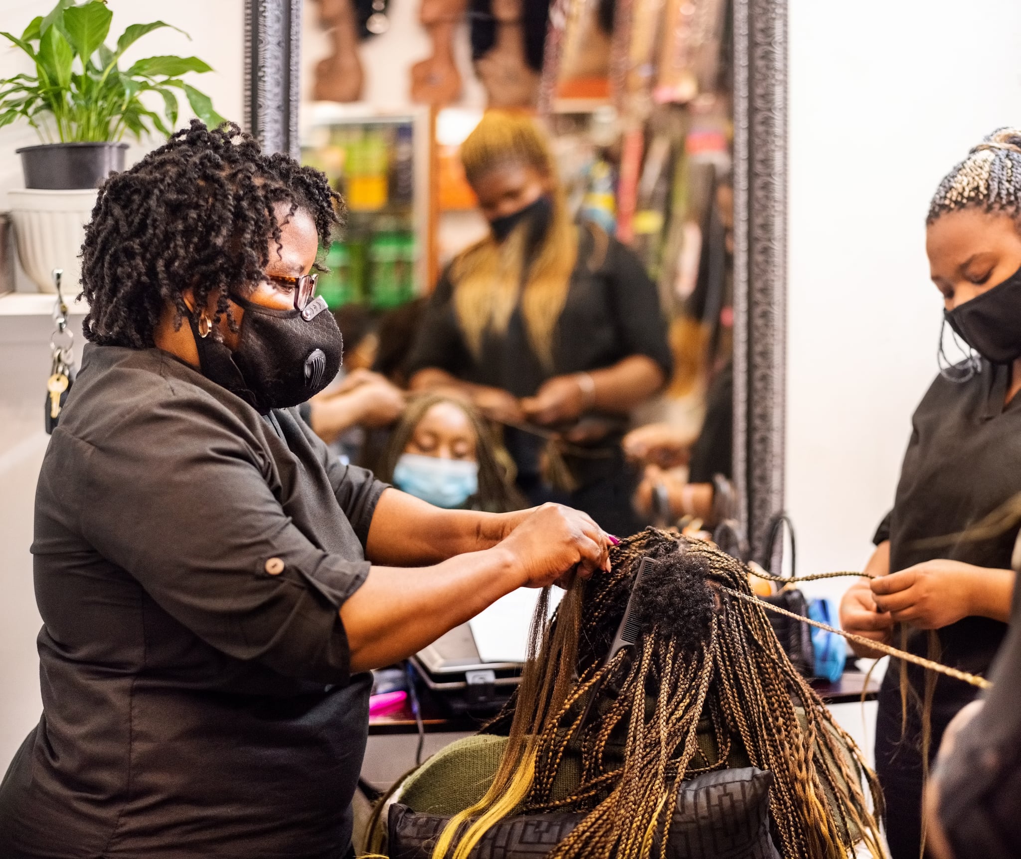 Hairstylists braiding and extending a client's hair in salon.