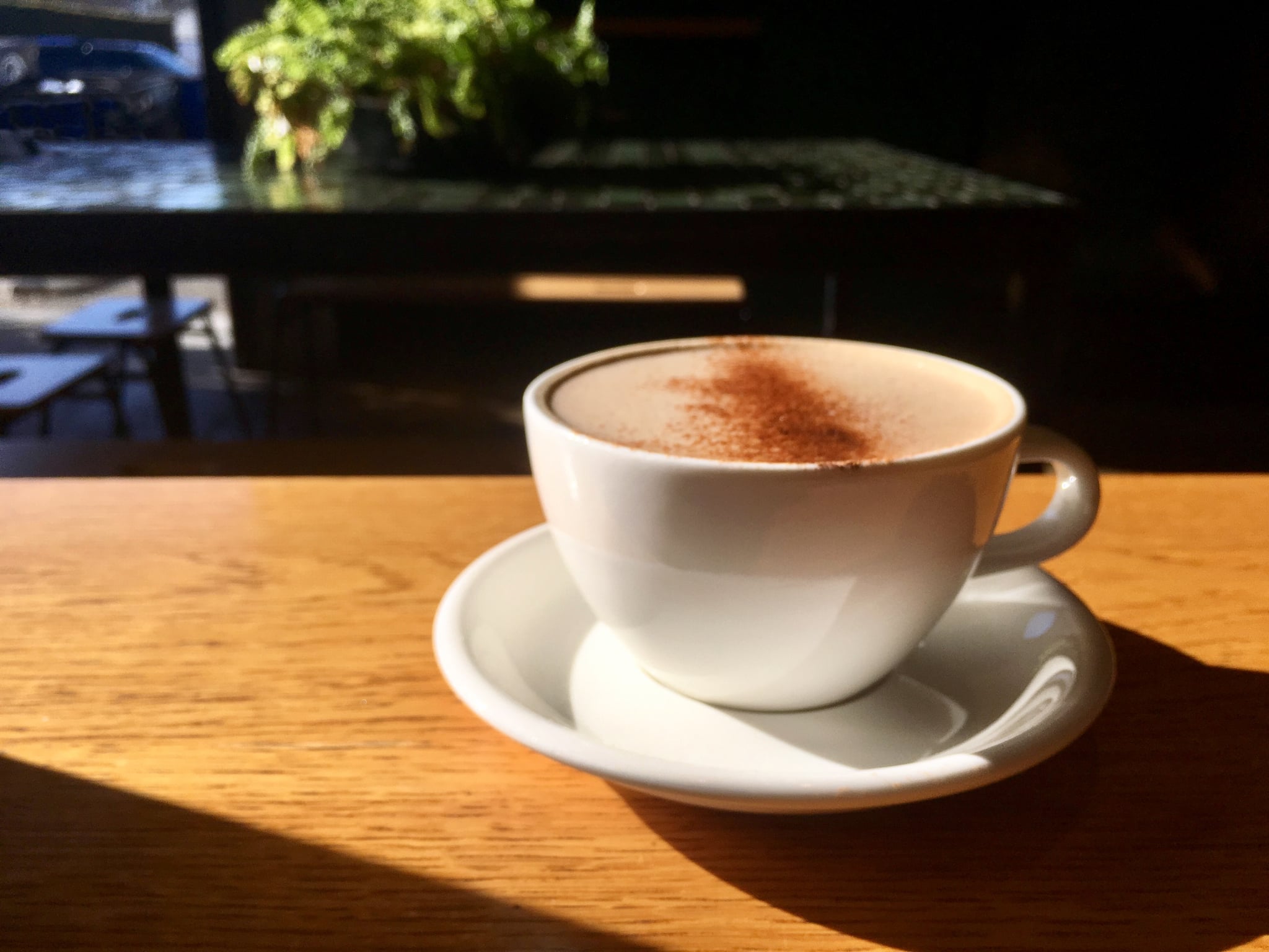A gourmet chai latte, topped with cinnamon, in a white ceramic cup sits in sunlight on a wooden table-top on an outdoor patio in Los Angeles, CA. The best chai concentrate recipe lets you recreate this at home.