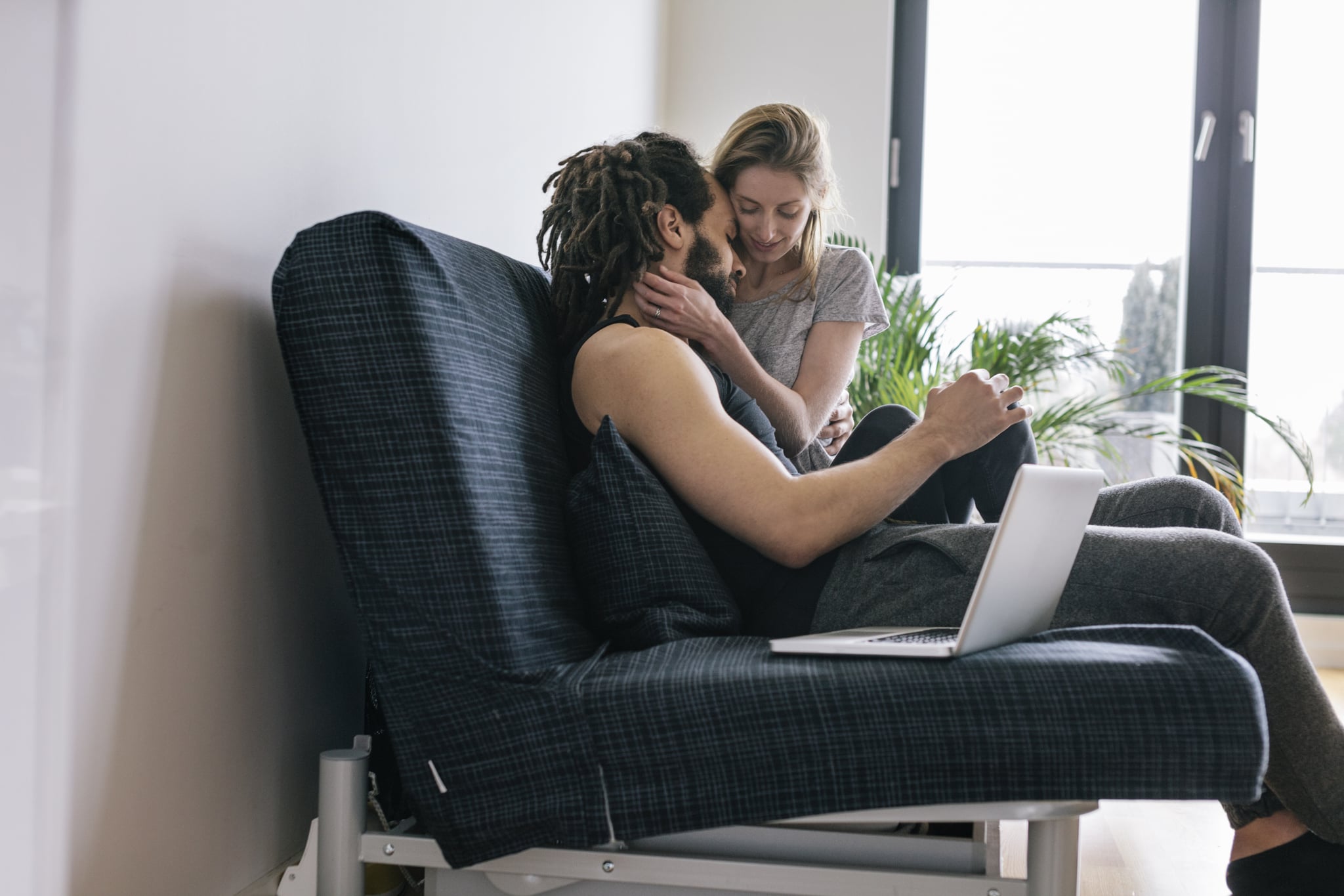 Interracial  Couple sitting on Sofa sharing tender moment. Laptop computer is sitting next to the couple.