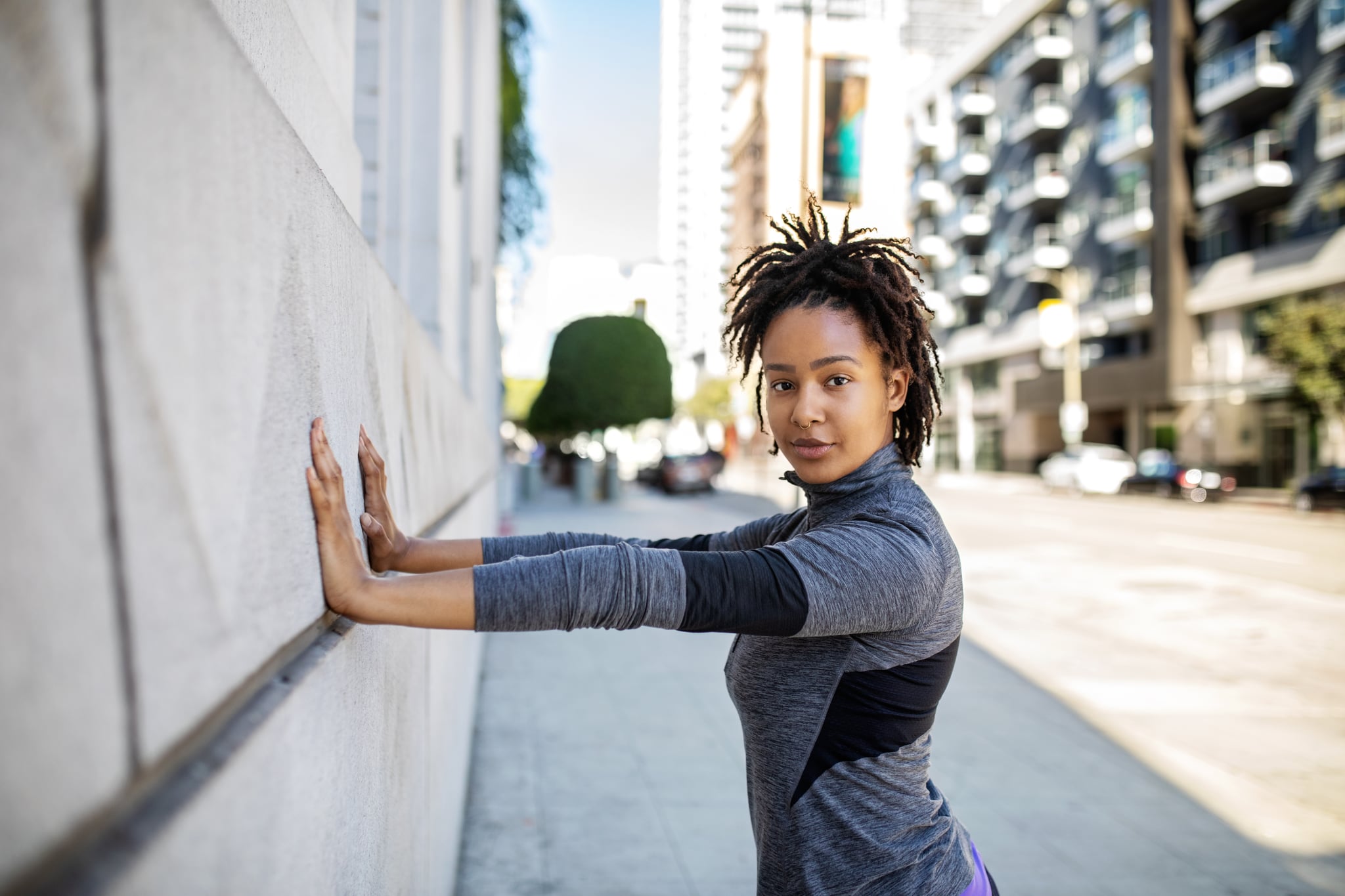 Portrait of a fit young african woman doing stretching workout against a wall. Fitness female exercising in morning outdoors.