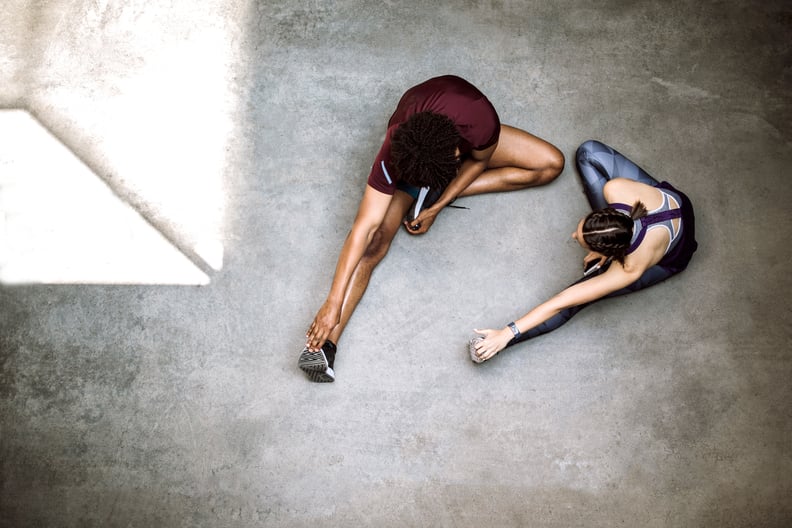 Attractive woman and handsome Afro man sitting on floor, stretching before morning jogging