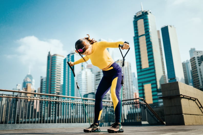Young Asian sports woman exercising with a resistance band outdoors, with urban city skyline as background