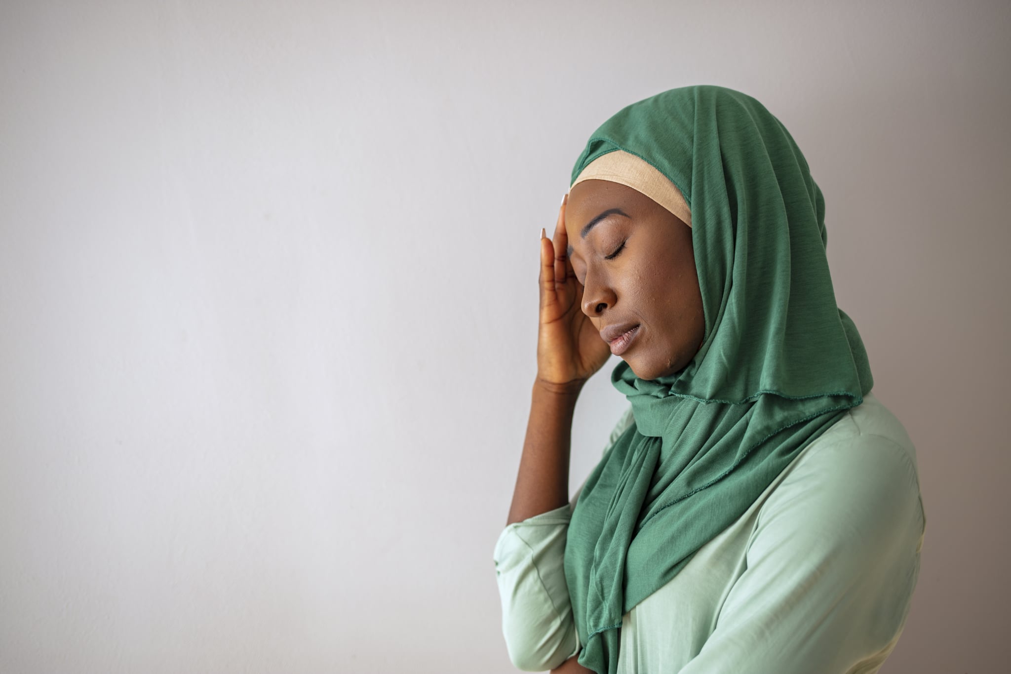 Muslim woman wearing hijab with hand on head.