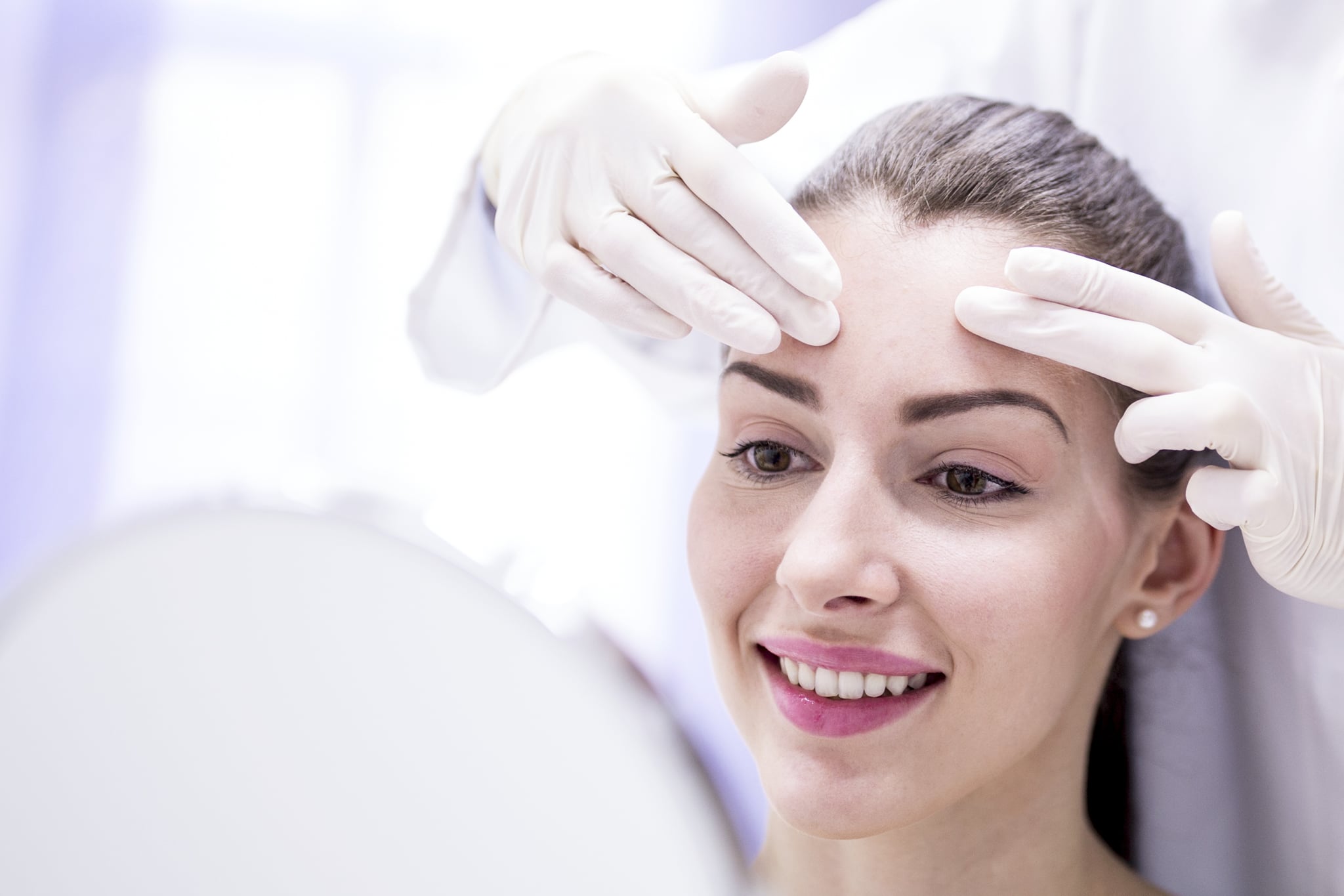 Doctor examining young woman's forehead.