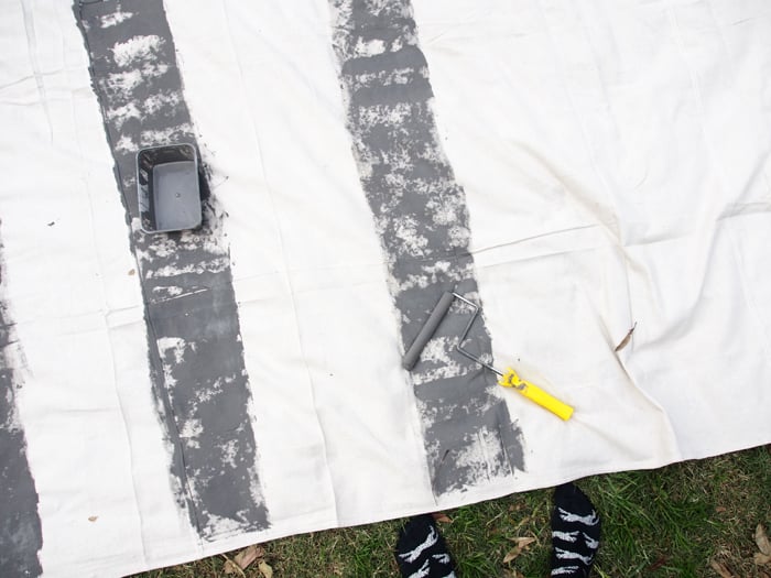 Unless you have a surplus supply of drop sheets you can lay down, it’s a good idea to set up somewhere you can spill a lil paint without getting in trouble, like your back lawn or local park!
Start by rolling out horizontal stripes with your widest roller. These stripes will be the base of the tartan pattern, so I think it’s good to start with a neutral so your other colors will pop out against them. And don’t mind my leopard socks, I took my shoes off so I could step on the sheet without making any marks! :)