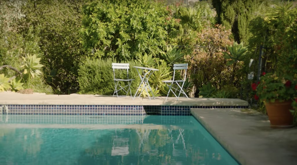 The porch is surrounded by trees and potted plants, and a simple two-seater table set is situated by the pool.