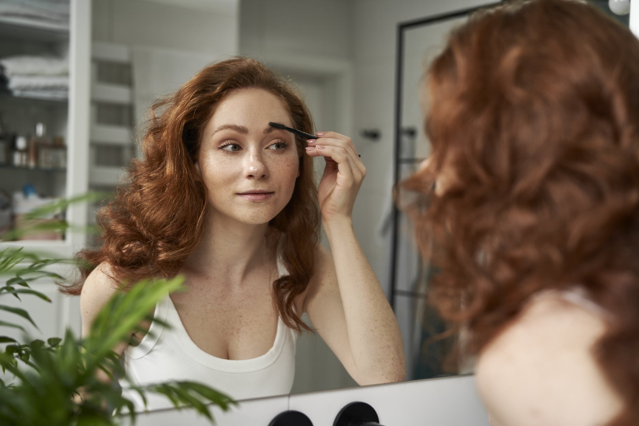 Caucasian woman brushing eyebrows in the mirror reflection