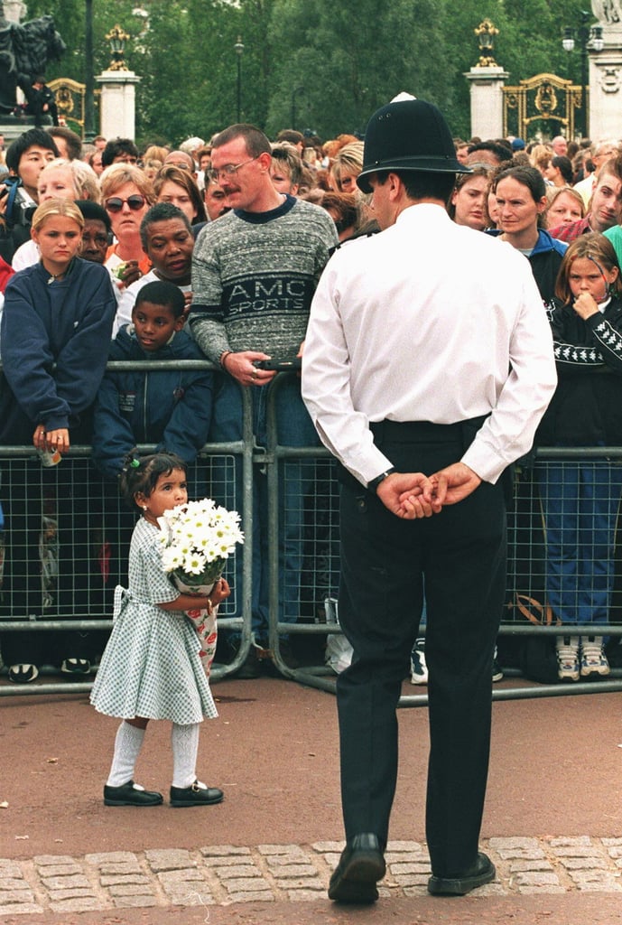 A little girl holding flowers looked up at a police officer in front of Buckingham Palace.
