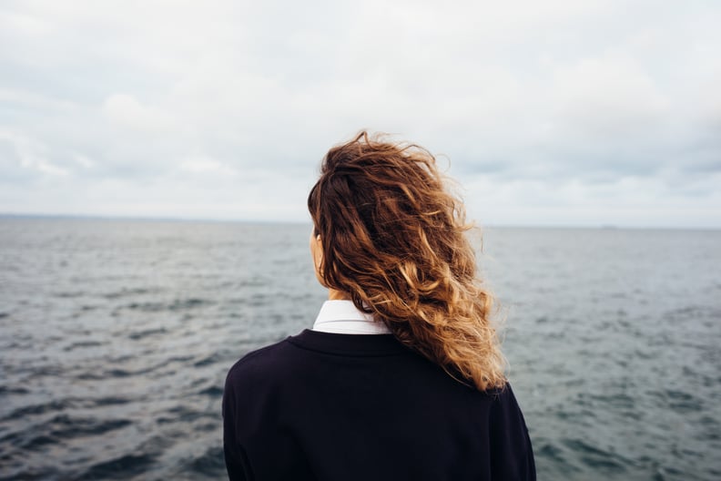 后视图的年轻女子看着阴暗的天空,灰色的海。女性用红色卷发孤独思考背景的海景。
