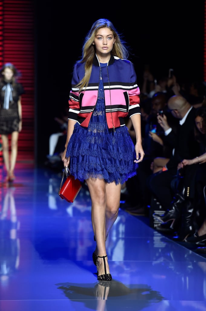 Gigi wore a cobalt blue minidress that featured tiered lace ruffles and sheer details. Just as a street style star would, Gigi contrasted the feminine design with a colorblock bomber jacket fit for a cool girl. Her outfit was complete with a bright red satchel and T-strap pumps.