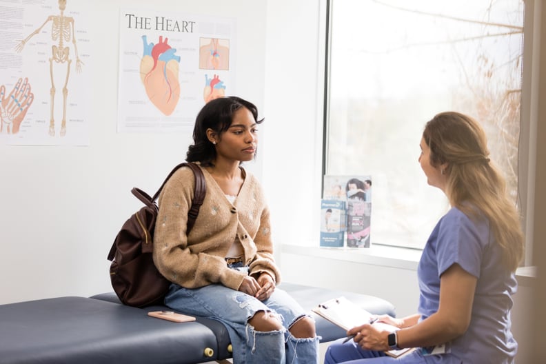The female doctor sits with the young adult female patient to review her medical history before asking about her most recent symptoms.