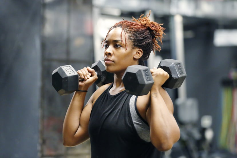 Wasit up image of a fit, young African American woman working out with hand weights in a fitness gym.