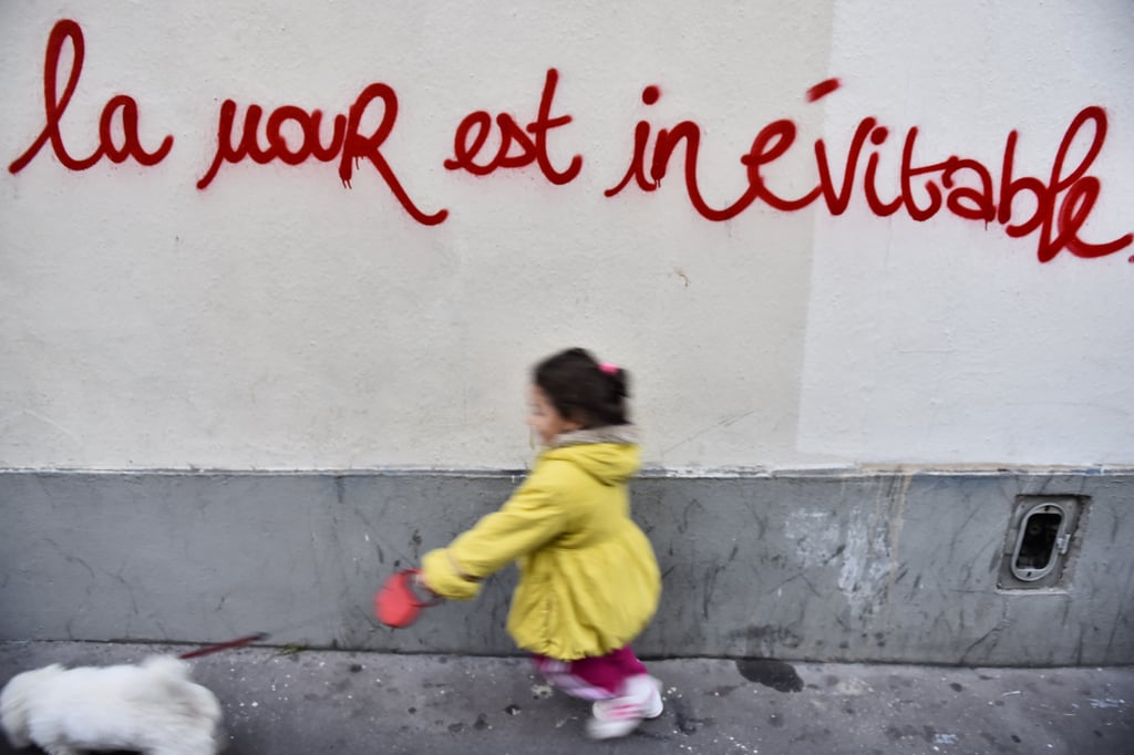 A young girl walked a dog in front of graffiti with the message "love is inevitable" in Paris.
