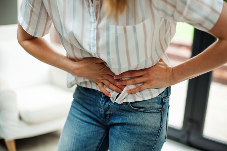 Woman wearing a white striped shirt and jeans bent over holding her stomach