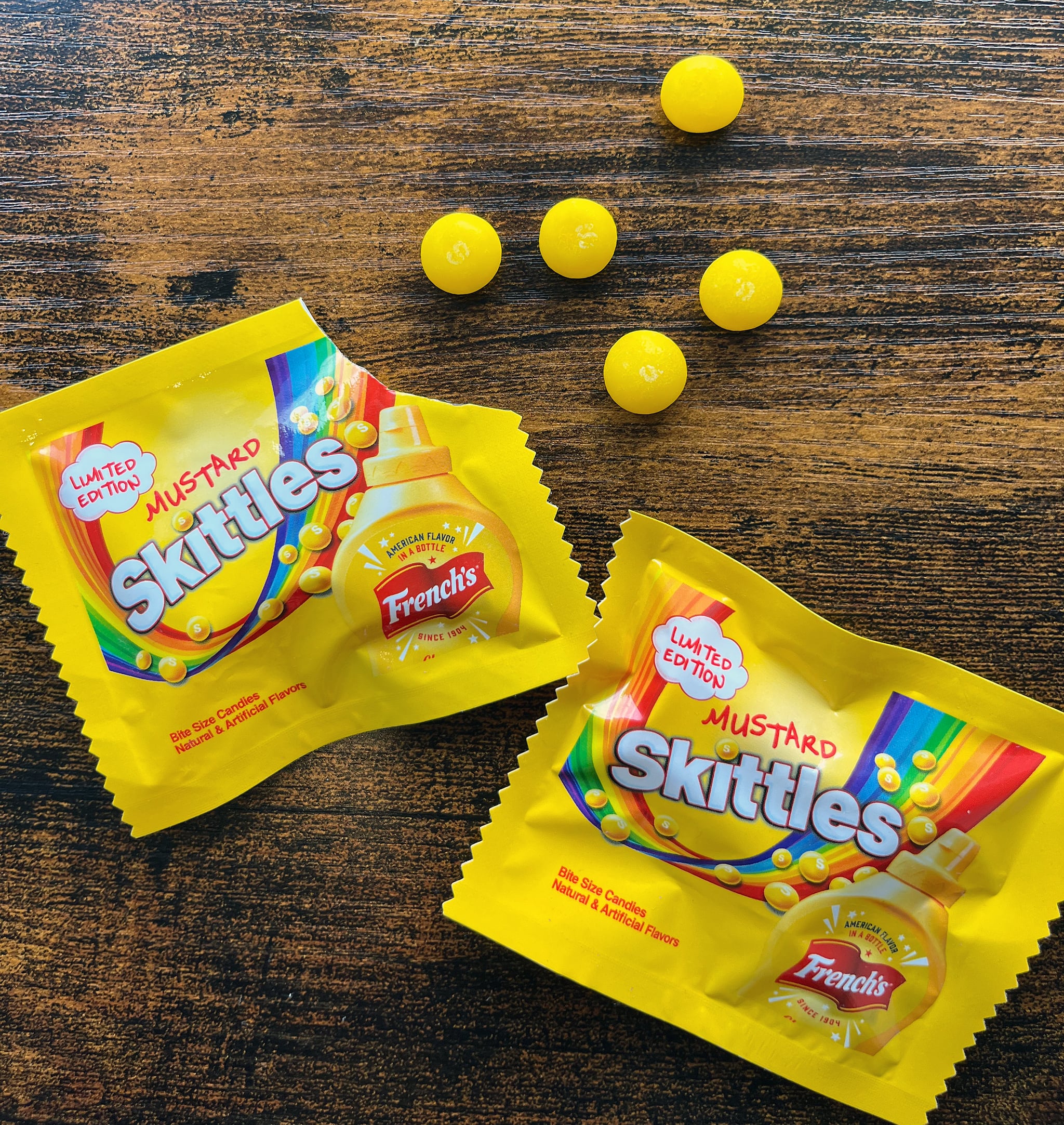 Two packages of French's mustard-flavoured Skittles candies.