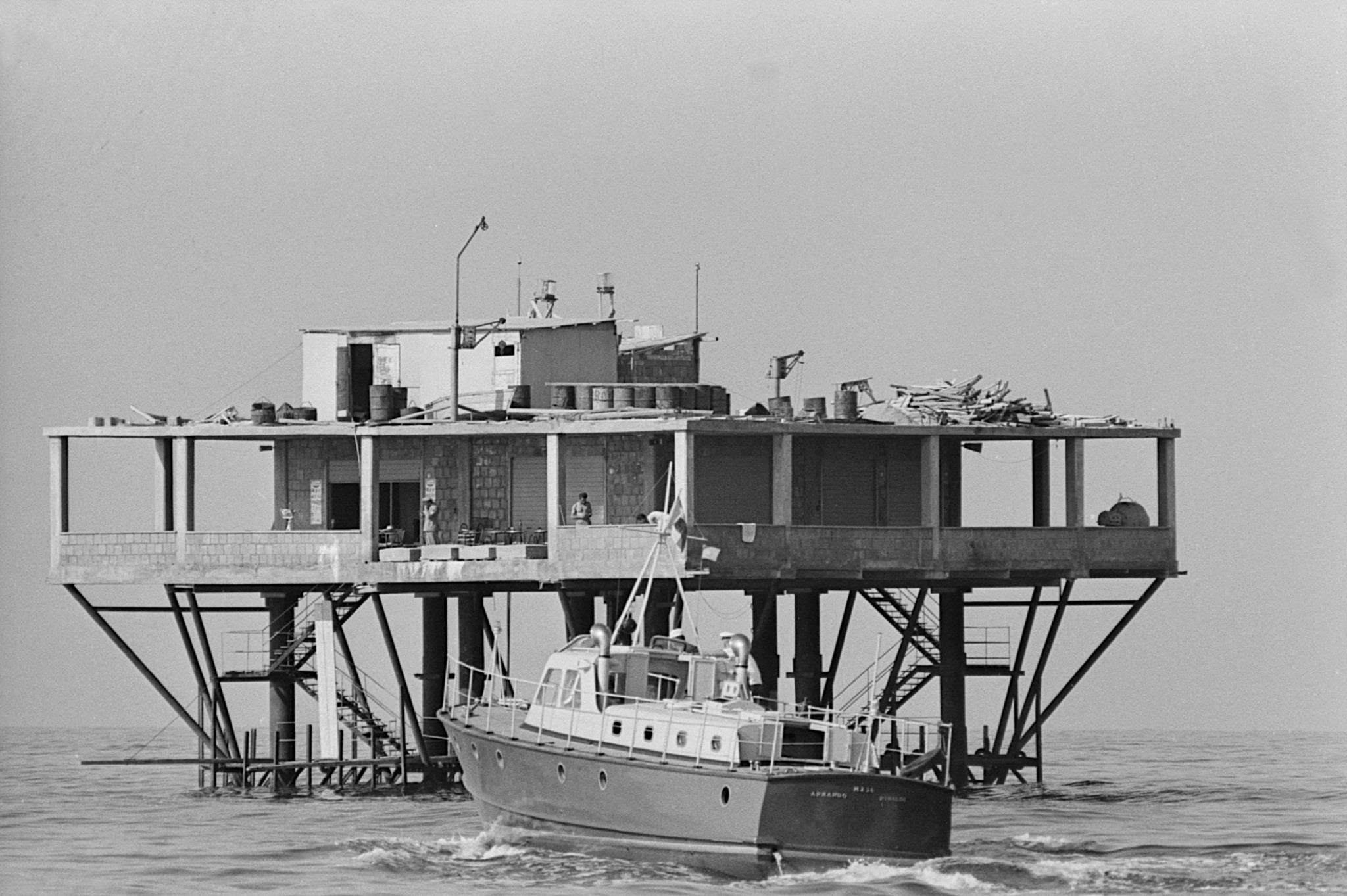 Pietro Bernardini lives in the steel and concrete platform which rises 11 km and 600 m off the coast of Rimini. At the moment, he is the only inhabitant of the island, rented for a year. The building begun in 1964, it rises above 9 steel pillars filled with concrete. It covers an area of 400 sqm, outside the Italian territorial waters. The creator and builder is engineer Giorgio Rosa. The Police motorboat monitors the island because the Italian government doesn't recognise its sovereignty. Italy, July 1968 (Photo by Giuseppe Pino\Mondadori Portfolio\Mondadori via Getty Images)