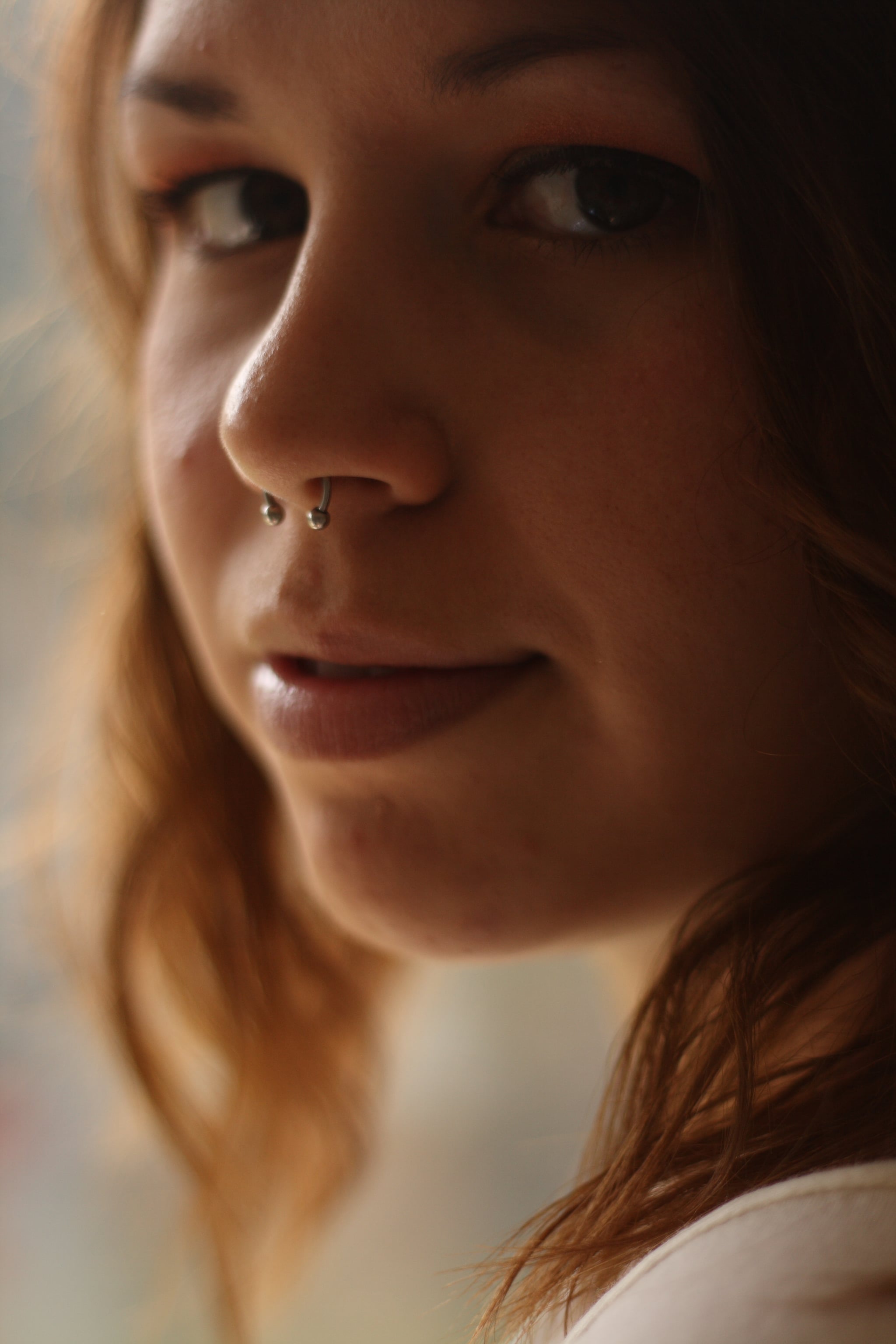 Young girl looking over her shoulder with a peaceful look on her face. Body modification of a septum ring hangs from her nose.