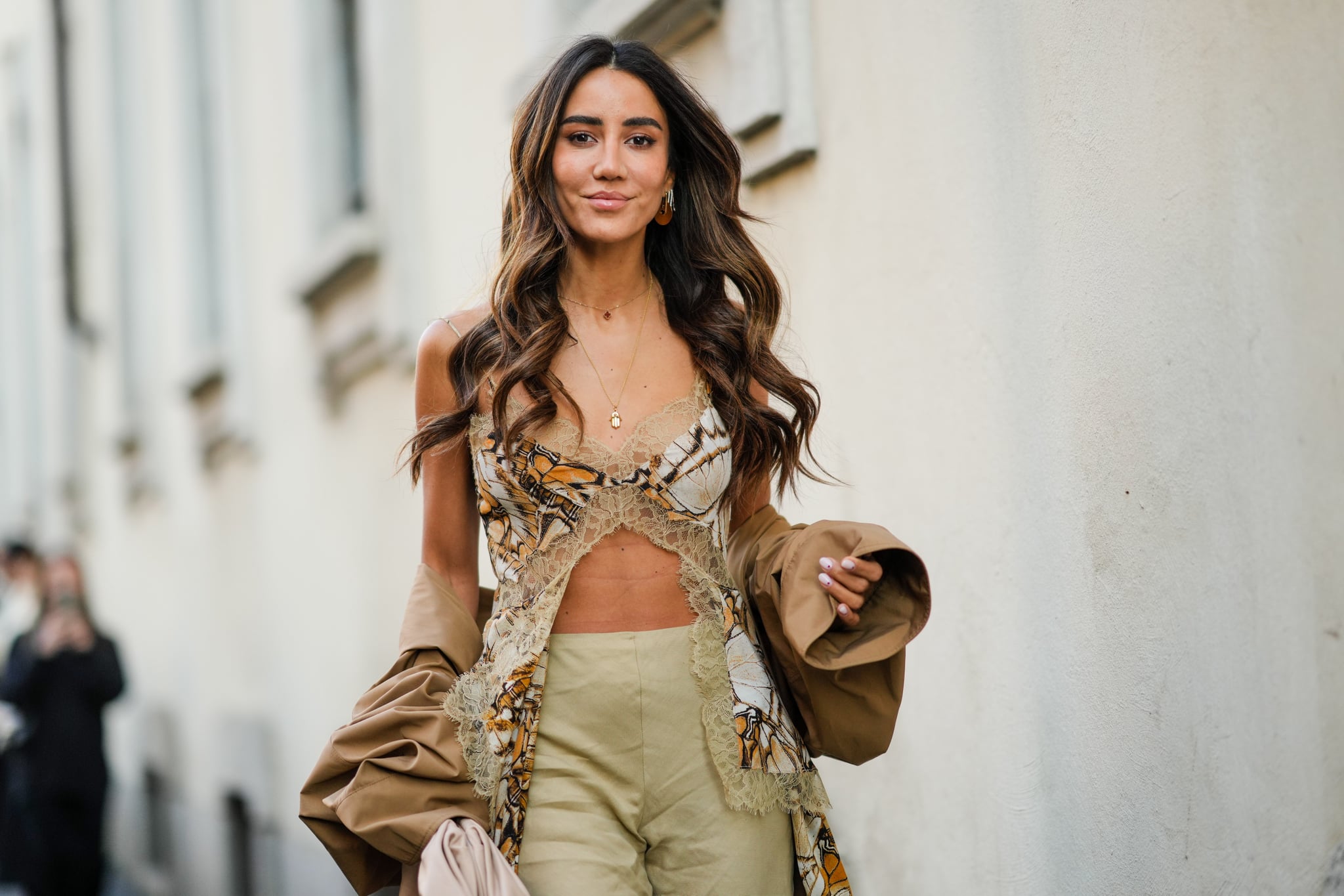 MILAN, ITALY - FEBRUARY 23: Tamara Kalinic wears gold long chain necklaces, a brown oversized long coat, a brown / white / orange print pattern V-neck / cut-out with borders lace embroidered pattern t-shirt with long train, high waist khaki wide legs pants, a beige matte leather puffy handbag from Bottega Veneta, outside the Alberta Ferretti fashion show, during the Milan Fashion Week Fall/Winter 2022/2023 on February 23, 2022 in Milan, Italy. (Photo by Edward Berthelot/Getty Images)