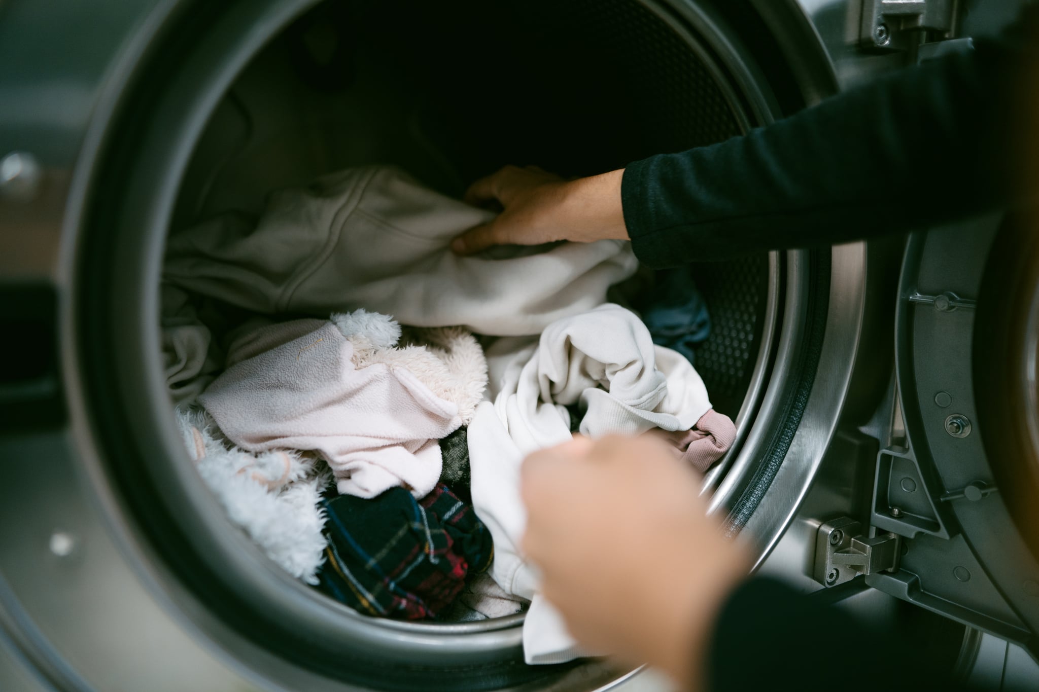 Young  woman hands putting her dirty clothes in the washing machine in a laundromat.
