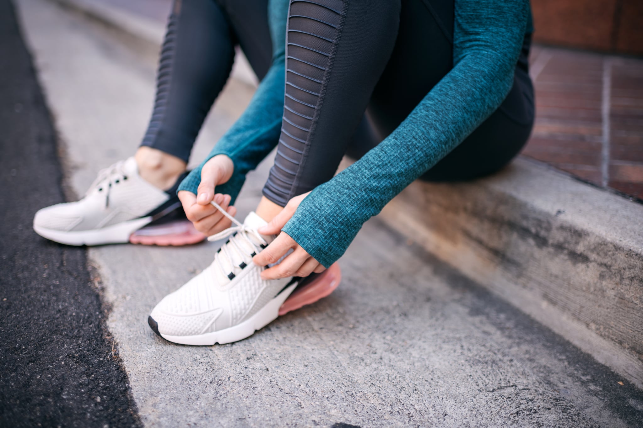 Strong active woman tying her shoelace while  sitting on the street sidewalk.