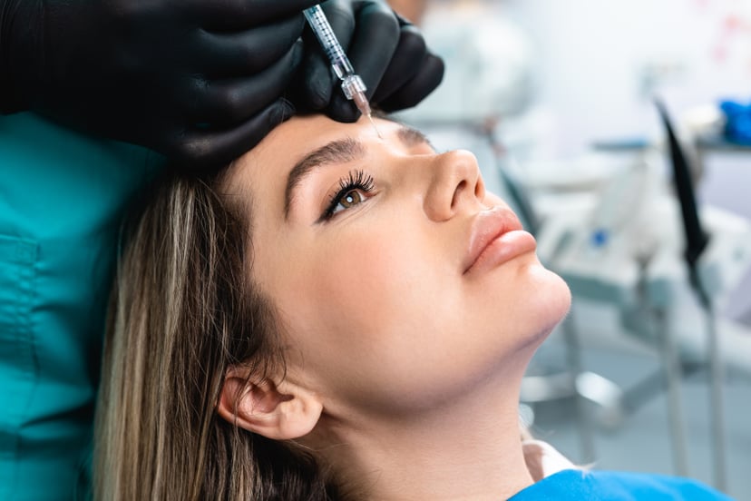 Attractive young woman is getting a rejuvenating facial injections at beauty clinic. The expert beautician is filling female wrinkles by botulinum.