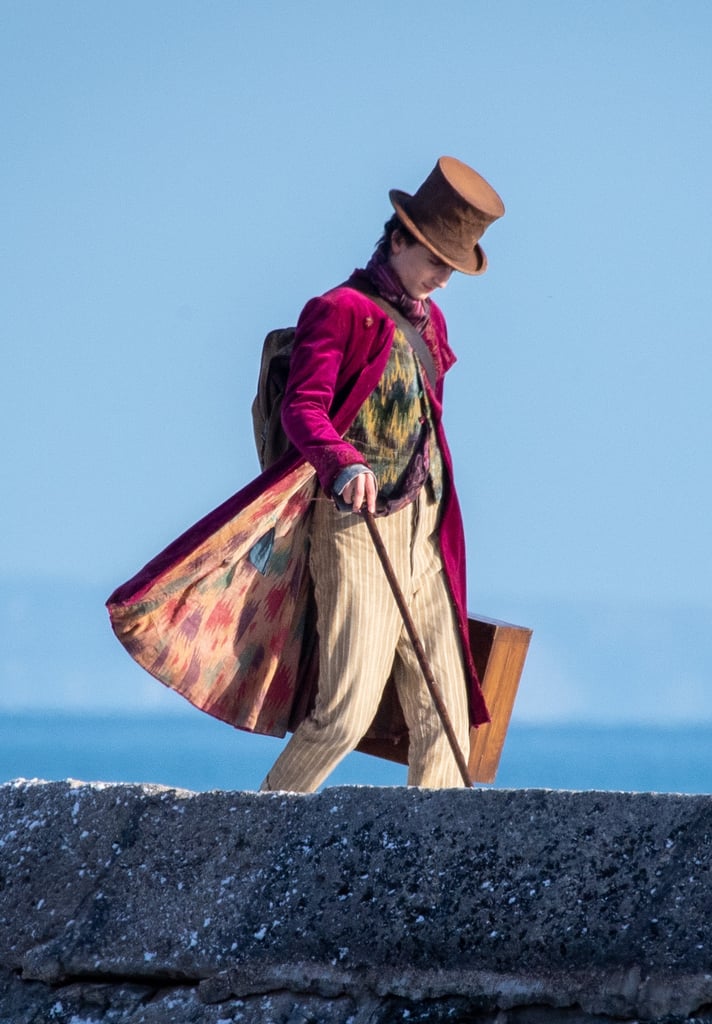 Shout-out to the breeze in England for revealing the colorful underside of Timothée's Wonka coat. As for the layers underneath, he was rocking a pink-and-purple patterned scarf tucked into a black-and-mustard button-up waistcoat.