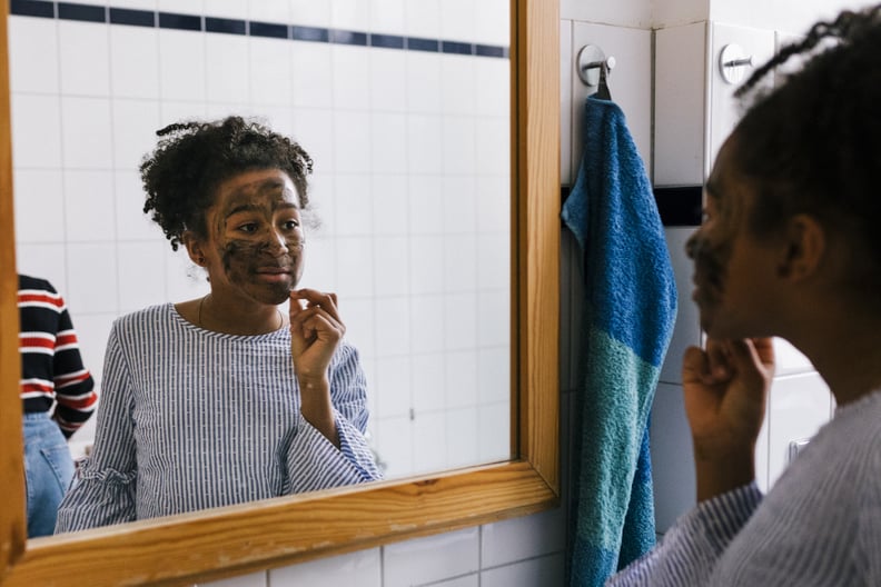 Black tween in applying facial mask while looking into a bathroom mirror.