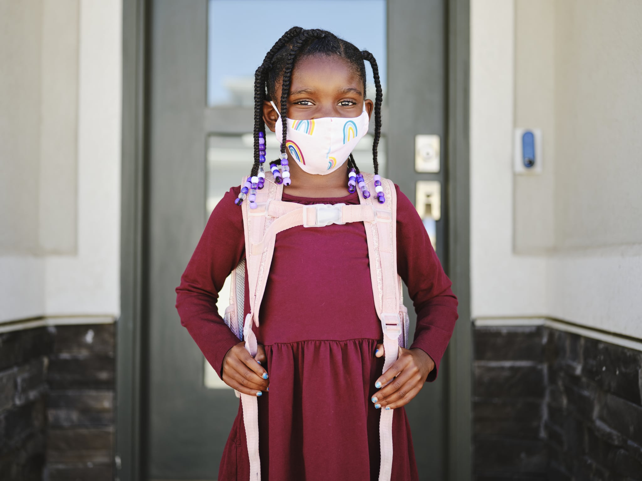 An elementary aged school student leaving her home to go back to school, wearing a mask for protection against infectious disease.