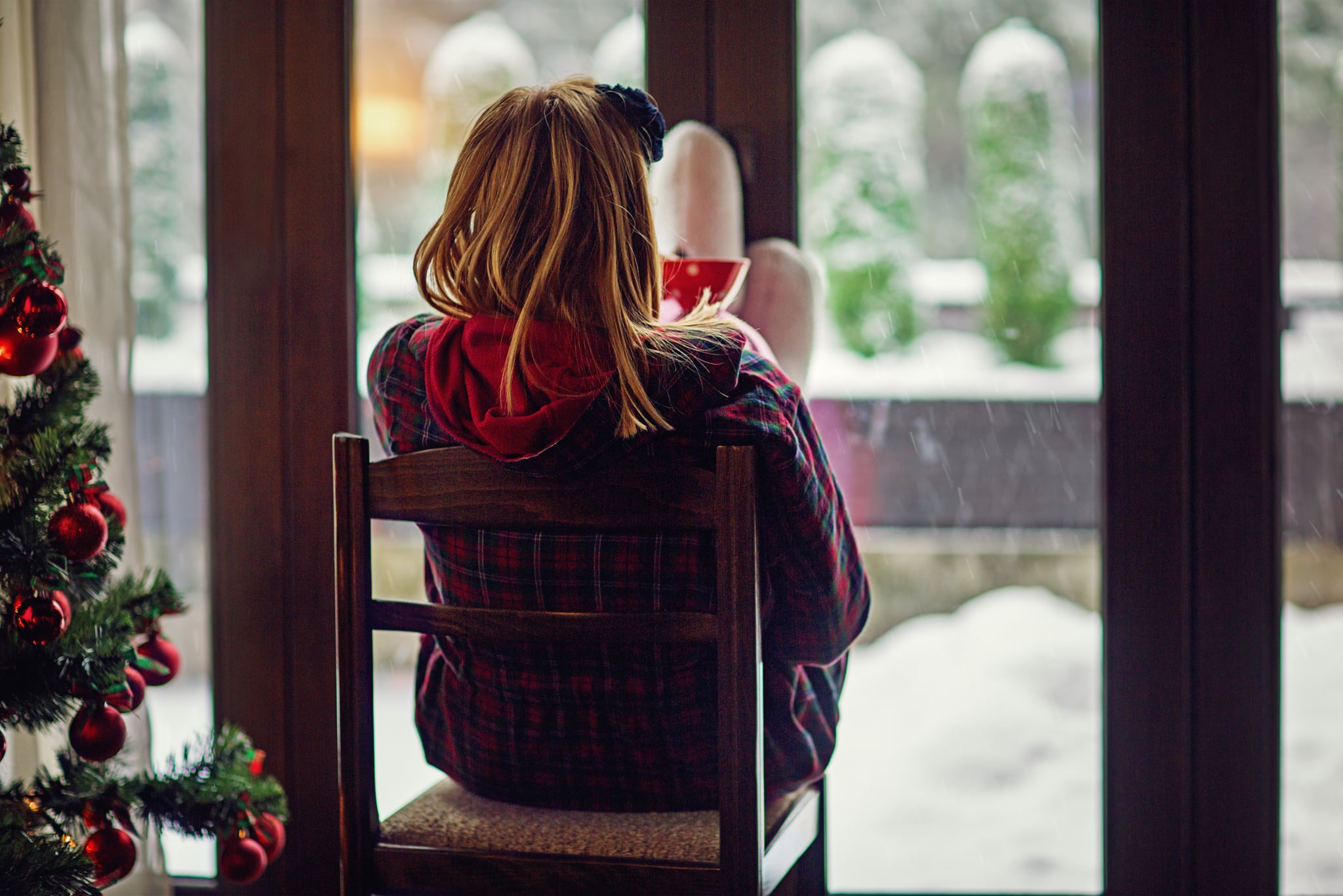 Young woman is looking the falling snow outside