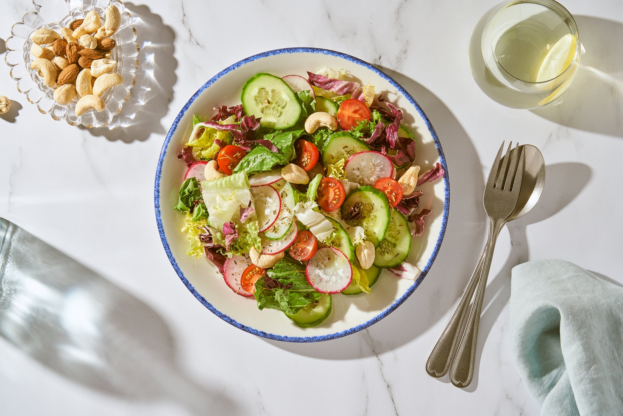 a plate of salad next to a bowl of mixed nuts