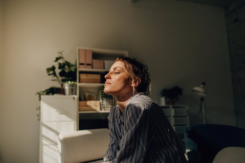 a woman sitting in her bedroom closing her eyes as sunlight hits her face