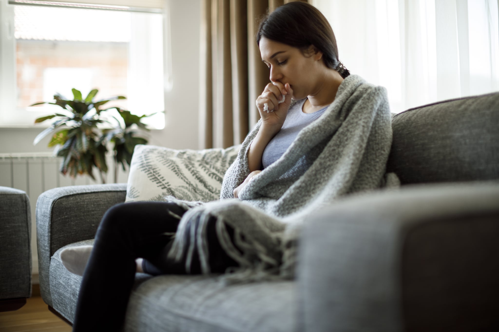 Woman sitting on the couch coughing.