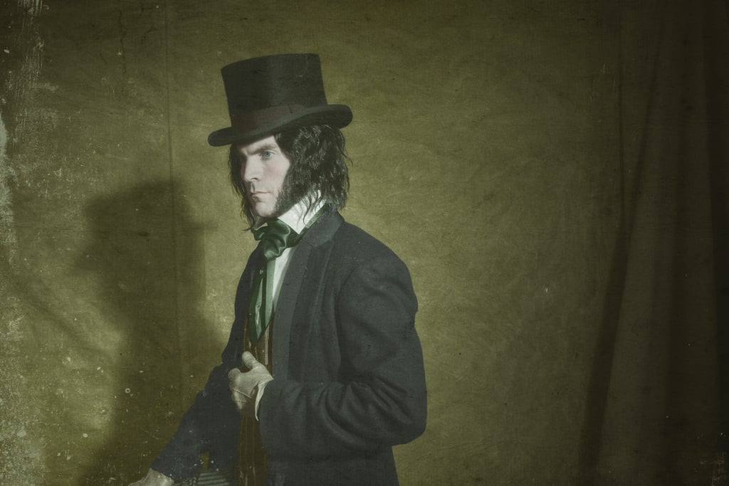  A man wearing a top hat and a green cravat is standing in front of a green wall.