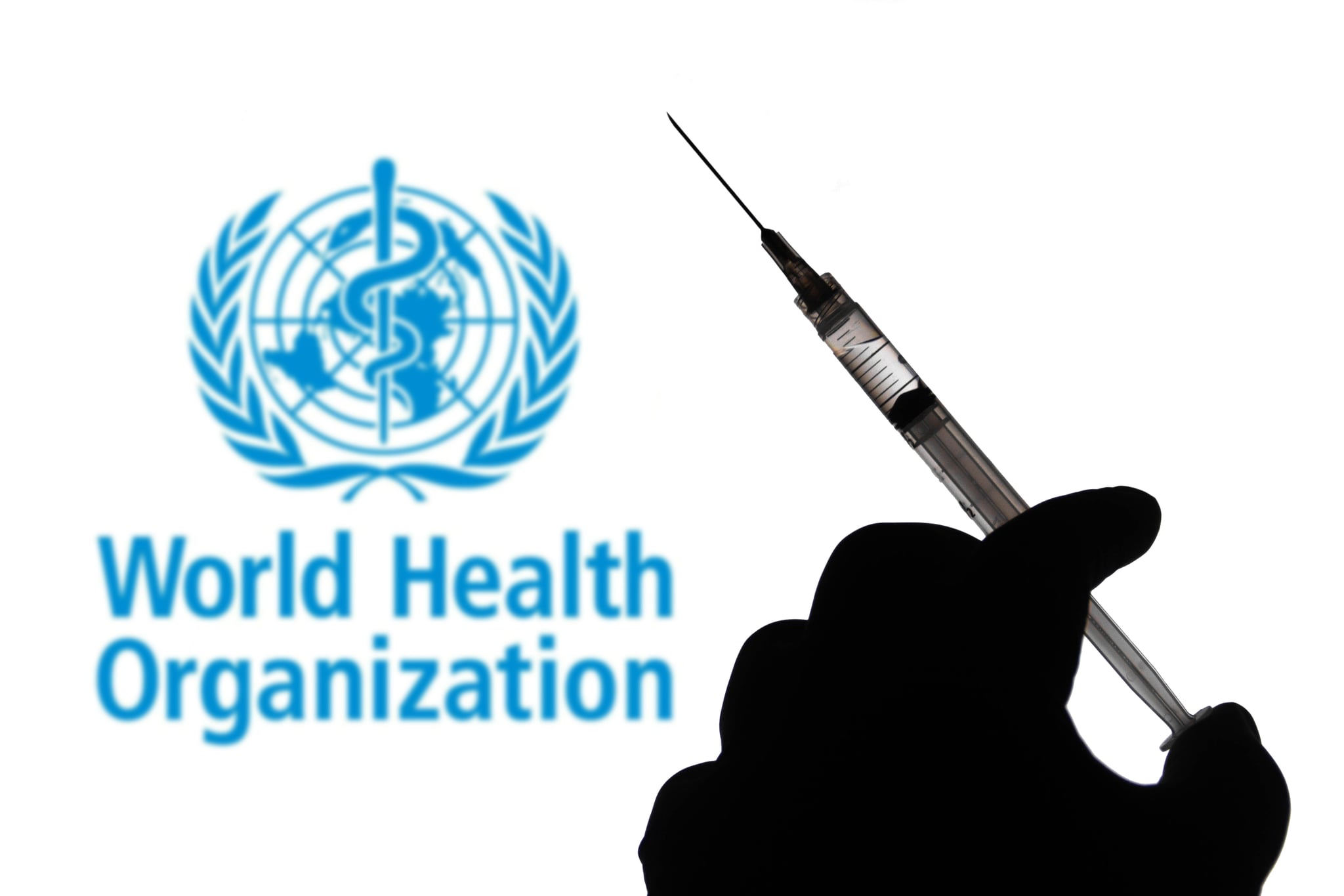 BRAZIL - 2021/04/02: In this photo illustration, a hand holds a medical syringe with a World Health Organisation (WHO) company logo displayed on a screen in the background. (Photo Illustration by Rafael Henrique/SOPA Images/LightRocket via Getty Images)