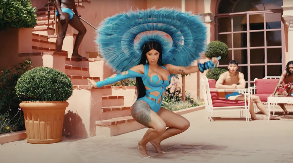 In the following scene, she changes into a blue Julian Méndez Couture one-piece with intricate cutout details and a matching feathered headpiece by Harris Reed. She ditches the heels to drop it low.