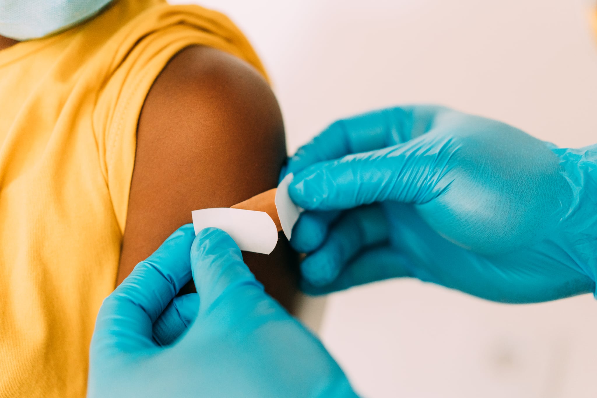 Male doctor putting a bandage on the arm of a little girl after giving Coronavirus/COVID-19 vaccine in the clinic. Close-up shot of a healthcare worker placing a bandage on a patient's arm after coronavirus vaccination.