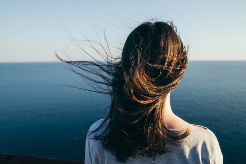 深色头发的女人站在一个悬崖顶部蓝色海景而风。