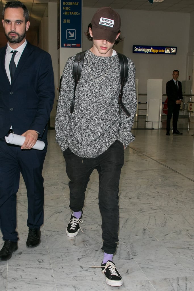 Keeping his airport style casual in a grey sweater, a dad hat, purple socks, and sneakers.